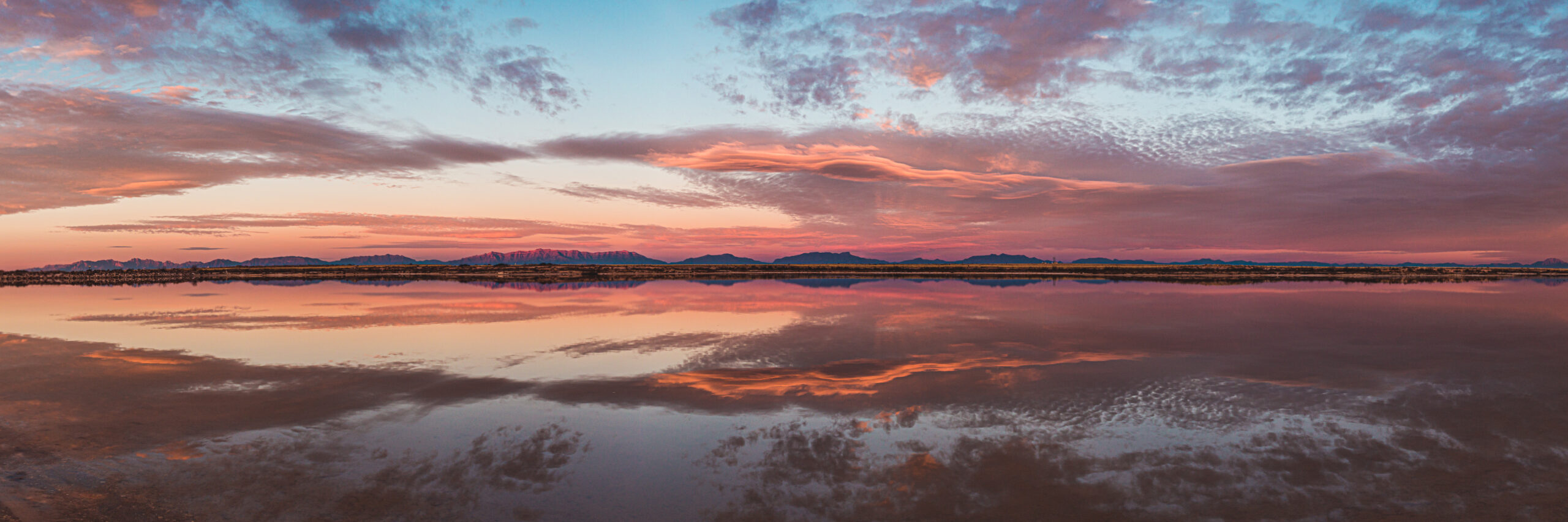 Panoramic sunset view from Santa Fe Baldy showing vibrant red, orange, and purple skies over layered mountain ridges and rocky foreground.